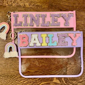 May include: Two clear plastic zippered pouches with colorful felt letters spelling out the names "Linley" and "Bailey". Each pouch has a rainbow-colored tassel keychain attached.