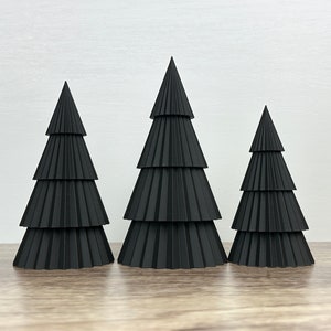Puede incluir: Tres árboles de Navidad de papel negro de diferentes tamaños. Los árboles están hechos de papel doblado y tienen un diseño en capas y escalonado.