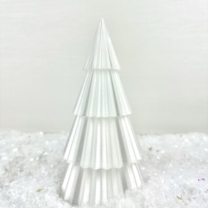 Könnte beinhalten: Ein weißer, papierner Weihnachtsbaumschmuck mit plissiertem Design. Der Schmuck liegt auf einem Bett aus weißem Glitzer.