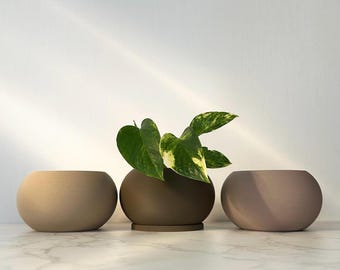 May include: Three round ceramic planters in beige, brown, and light pink. A green potted plant is in the middle planter.