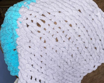 Puede incluir: Una manta de punto suave y gruesa en color gris y turquesa. La manta está colocada sobre un sillón de cuero marrón.