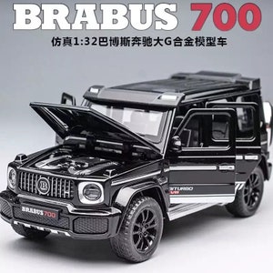 Puede incluir: Un coche modelo de fundición a escala 1:32 de color negro de un Brabus 700 Mercedes-Benz Clase G con el capó abierto, revelando el motor. El coche tiene un acabado plateado y las palabras "BITURBO V8" en el lateral.