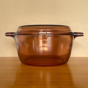 May include: A brown glass casserole dish with a lid and two handles. The dish is on a wooden surface.