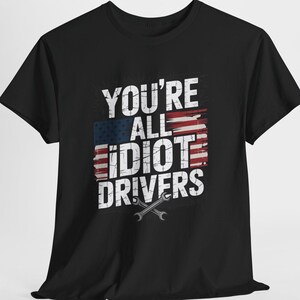 May include: Black t-shirt with the text "YOU'RE ALL IDIOT DRIVERS" in white, with a distressed American flag design. Two crossed wrenches are at the bottom of the graphic. A crew neck tee.