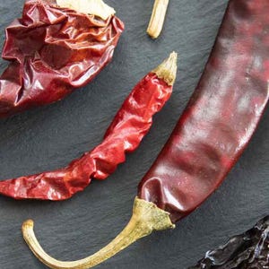 May include: Dried red chili peppers of various sizes and shapes, including a large, dark brown dried chili pepper.