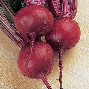 May include: Three red beets with green leafy tops. The beets are round and smooth with a deep red color.