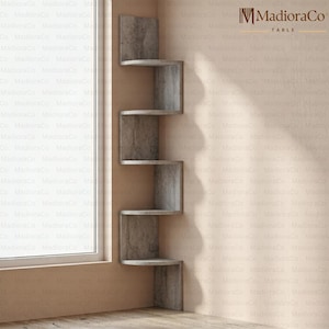 May include: A gray, zig-zag corner shelf unit with five shelves. The shelves are made of a material that resembles concrete. The unit is mounted on a wall next to a window. The brand name "MadioraCo" is visible.