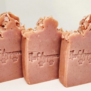 May include: Three bars of pink soap with the text "Hoof Approved" and a paw print design. The top of each bar has a textured, light brown, frosting-like design. The soap is on a white background.