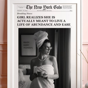 Pu&ograve; includere: Una fotografia in bianco e nero di una donna avvolta in un asciugamano bianco, che tiene una tazza di caff&egrave;. La foto &egrave; incorniciata e ha un titolo di giornale che recita "La ragazza si rende conto che in realt&agrave; &egrave; destinata a vivere una vita di abbondanza e facilit&agrave;."