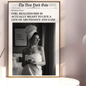 Pu&ograve; includere: Una fotografia in bianco e nero di una donna avvolta in un asciugamano bianco, che tiene una tazza di caff&egrave;. La foto &egrave; incorniciata e ha un titolo di giornale che recita "GIRL REALIZES SHE IS ACTUALLY MEANT TO LIVE A LIFE OF ABUNDANCE AND EASE".