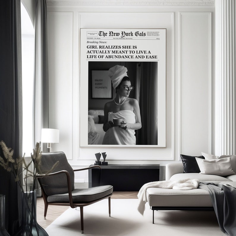 Pu&ograve; includere: Foto in bianco e nero di una donna avvolta in un asciugamano, che tiene una tazza di caff&egrave;. La foto &egrave; incorniciata e appesa a una parete in un soggiorno moderno. Il testo sulla foto recita "The New York Gals" e "Breaking News: GIRL REALIZES SHE IS ACTUALLY MEANT TO LIVE A LIFE OF ABUNDANCE AND EASE."