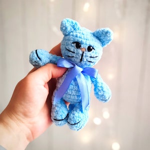 Peut inclure: Un jouet en crochet en forme de chat bleu clair avec un ruban bleu. Le chat a des yeux et des moustaches brodés noirs.