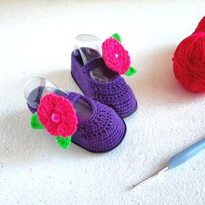 Pu&ograve; includere: Un paio di scarpine per neonati in crochet viola con decorazioni floreali rosa. Le scarpine sono fatte a mano e hanno un design delicato e femminile.
