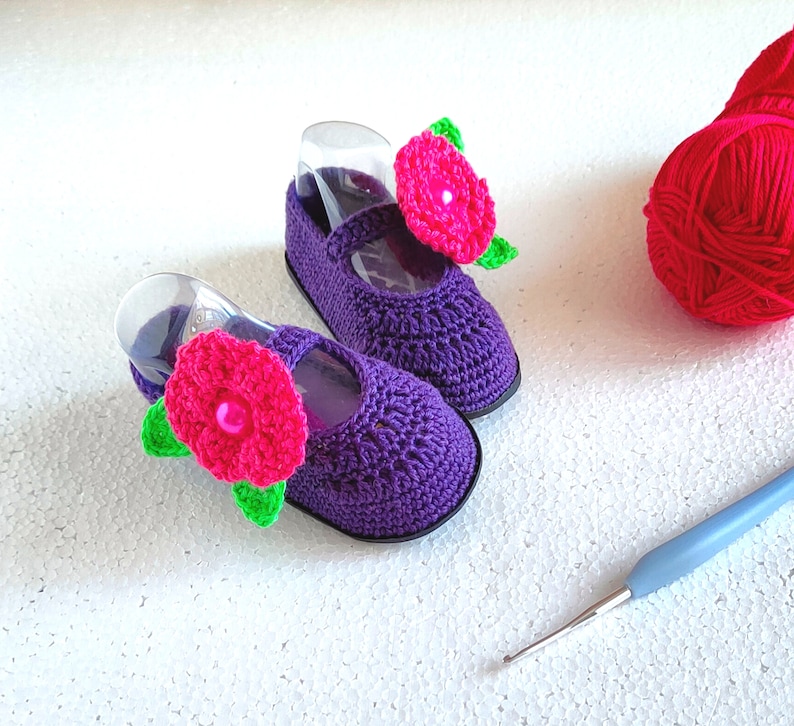 Pu&ograve; includere: Un paio di scarpine per neonati in crochet viola con decorazioni floreali rosa. Le scarpine sono fatte a mano e hanno un design delicato e femminile.