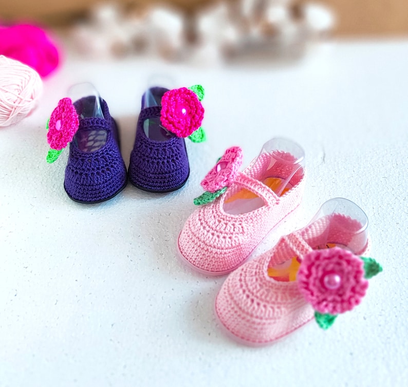 Pu&ograve; includere: Due paia di scarpine per neonati all'uncinetto con fiori rosa e viola. Le scarpine sono realizzate con un filato morbido e hanno un delicato motivo floreale.