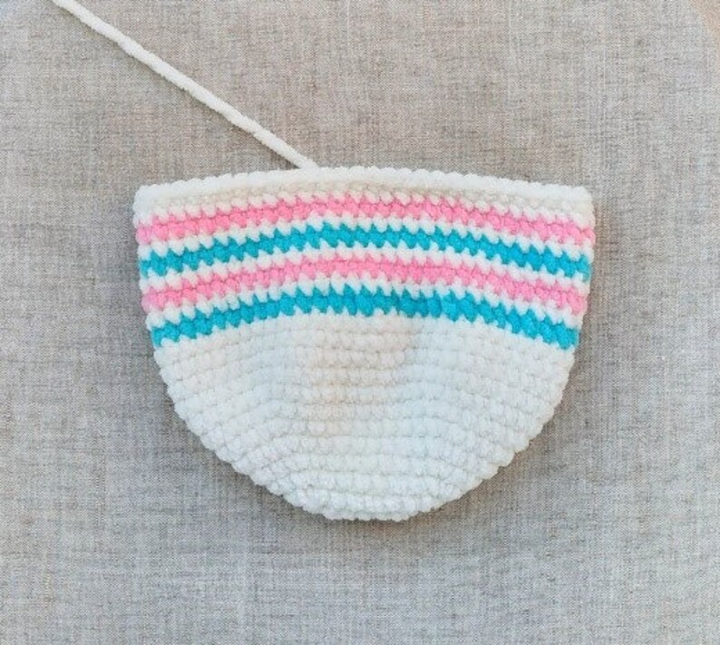 May include: A white crocheted bowl with pink and blue stripes. The bowl is made of a soft, fuzzy yarn.