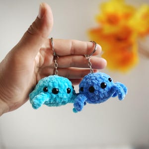 Puede incluir: Dos llaveros de pulpo tejidos a crochet, uno azul y otro turquesa, con ojos negros. Los llaveros cuelgan de llaveros plateados.