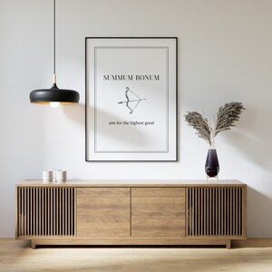 May include: A black and white print with the text "Summum Bonum" and an arrow pointing to the right. The text below the arrow reads "aim for the highest good". The print is hanging on a white wall above a wooden cabinet with two doors.