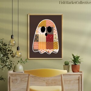 May include: A framed print featuring a patchwork ghost design. The ghost is white with a variety of autumn-themed fabric patterns in orange, brown, and cream. The artwork is set against a dark brown background and framed in gold, with the text "FishMarketCollective" at the top.