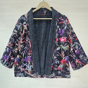 May include: A black quilted jacket with a floral print featuring birds and flowers. The jacket has a long sleeve and a relaxed fit.