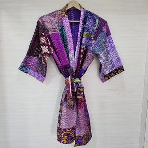 Könnte beinhalten: Eine violette und rosafarbene Patchwork-Seidenrobe mit einem Bindegürtel. Die Robe hat ein gestepptes Design und ist aus verschiedenen Stoffen gefertigt.