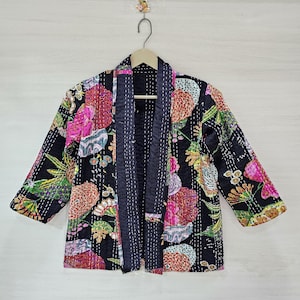May include: A black quilted jacket with a floral print in shades of pink, green, and yellow. The jacket has a long, open front and three-quarter sleeves.