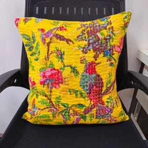 Könnte beinhalten: Ein gelbes Kissen mit Blumen- und Vogelmuster. Das Kissen ist gesteppt und hat eine quadratische Form.