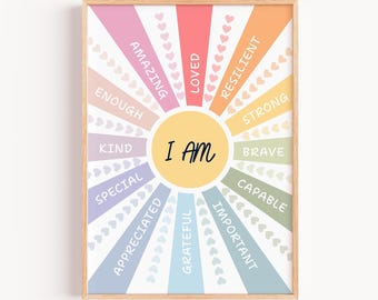May include: A framed print with a light wood frame. The artwork features a sunburst design with the words "I AM" in the center. Radiating from the center are colorful rays with positive affirmations like "Amazing," "Loved," and "Resilient."