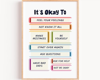 Op de afbeelding: Een ingelijste print met de tekst "It's Okay To" gevolgd door een lijst met affirmaties. De tekst is vetgedrukt, donkerblauw, met elke affirmatie in een ander gekleurd blok. De lijst is lichtbruin.