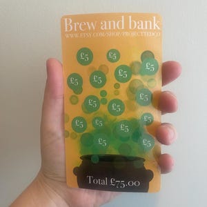 Puede incluir: Una tarjeta rectangular amarilla con el texto "Brew and bank" y la URL de la tienda Etsy. Presenta círculos verdes con el símbolo £5, un caldero y el texto "Total £75.00".