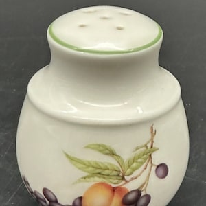 Peut inclure: Salerette en céramique blanche avec un bord vert et six trous sur le dessus. La salerette présente un motif peint de pêche, de raisins et de feuilles. Le corps est arrondi et le dessus légèrement évasé.