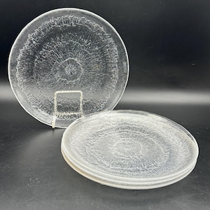 Könnte beinhalten: Klare Glasplatten mit einem strukturierten, radialen Muster. Eine Platte wird auf einem Metallständer präsentiert, während drei weitere gestapelt sind. Die Platten haben einen leicht erhöhten Rand und ein Sternmuster in der Mitte.