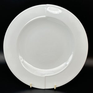 Könnte beinhalten: Ein weißer Keramik-Dinnerteller mit einem erhöhten Rand und einem leicht geschwungenen Design. Der Teller ist perfekt zum Servieren einer Vielzahl von Gerichten.