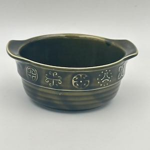May include: A dark green ceramic bowl with two handles. The bowl features a decorative band with embossed geometric patterns. The bowl has a round shape, suitable for serving soups, stews, or other dishes.