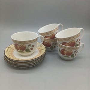 May include: A set of teacups and saucers. The cups and saucers are white with a decorative border and feature a design of peaches and berries. The saucers are stacked, and the cups are arranged in a group.