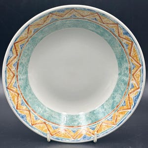 May include: A white ceramic bowl with a blue, green, orange, and yellow geometric pattern around the rim.