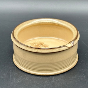 May include: A brown ceramic dish with a floral design and a small spout. The dish has a textured rim and a smooth interior.