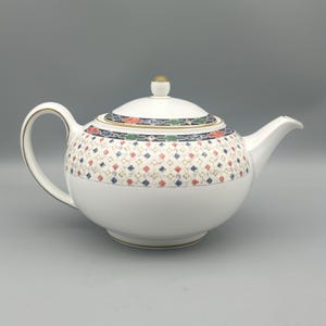 May include: White ceramic teapot with a pattern of red, blue, and gold diamonds. The lid and handle have gold accents. The teapot has a rounded body and a curved spout.