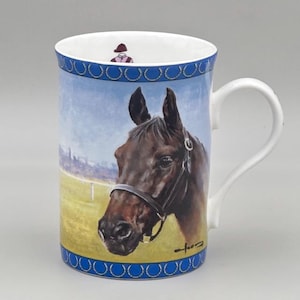 May include: White ceramic mug featuring a detailed painting of a brown horse's head with a bridle. The mug has a blue border with a repeating pattern and a small illustration of a jockey inside the rim.
