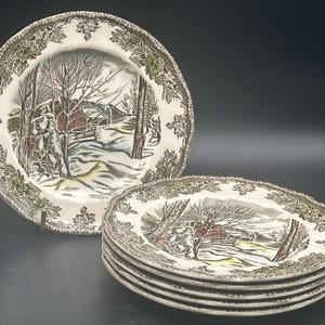 Könnte beinhalten: Satz von sechs braunen und weißen Keramik-Dinnertellern mit einem Wintermotiv. Die Teller haben einen braunen und weißen Rand mit einem grünen Blumenmuster. Die Mitte der Teller zeigt eine Winterszene mit einem Bauernhaus, Bäumen und Schnee.
