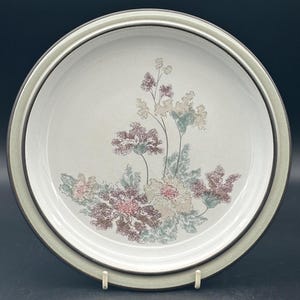 May include: A white ceramic dinner plate with a brown rim and a floral design in shades of pink, green, and brown.