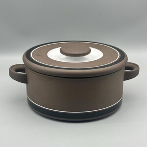 May include: A brown ceramic cooking pot with a lid. The pot has two handles and a white and black circular design on the lid. The pot is approximately 20 cm in diameter.