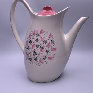 May include: White ceramic coffee pot with a pink lid and a floral design in shades of pink, blue, and gray.
