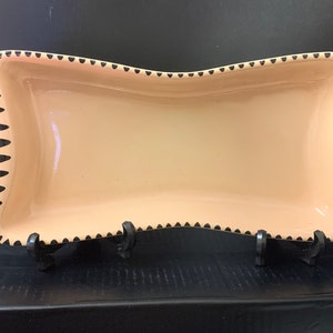 May include: A light pink ceramic serving dish with a wavy edge and black scalloped trim.
