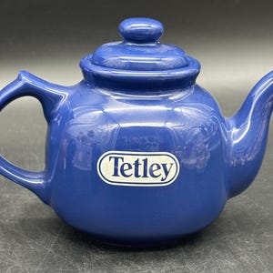 May include: A blue ceramic teapot with a white label that says "Tetley" on it.