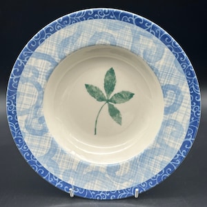 May include: A white ceramic bowl with a blue and white patterned border. The bowl has a green leaf design in the centre.