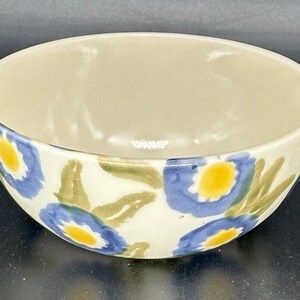 May include: A white ceramic bowl with a blue and yellow floral pattern. The bowl is round and has a slight lip.