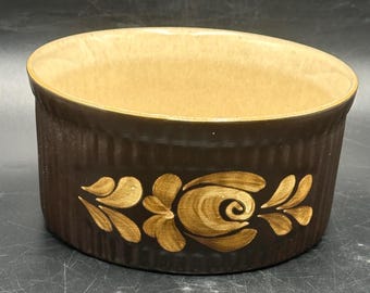 May include: A brown ceramic baking dish with a gold floral design. The dish has a textured exterior and a smooth interior.