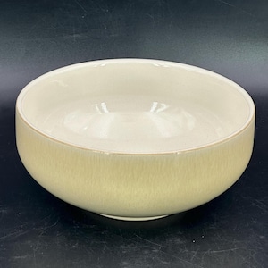 May include: A round, pale yellow ceramic bowl. The bowl has a smooth interior and textured exterior. It has a wide opening and a slightly darker rim. Likely for serving or display, it is a versatile kitchen item.