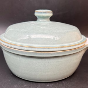 May include: A light blue ceramic casserole dish with a lid. The dish has a white rim and a gold trim around the top.